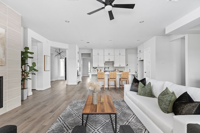 living room featuring a tile fireplace, light wood-type flooring, and ceiling fan