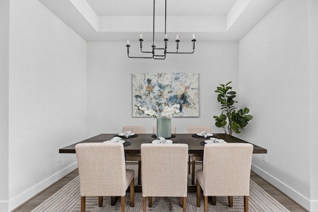 dining room featuring a tray ceiling, a notable chandelier, baseboards, and wood finished floors