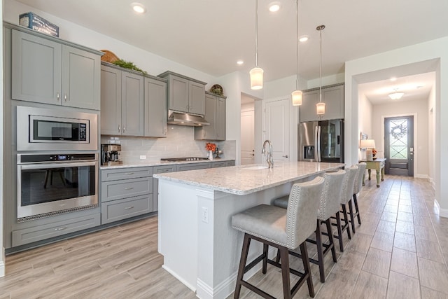 kitchen featuring light stone countertops, appliances with stainless steel finishes, hanging light fixtures, a breakfast bar area, and a center island with sink