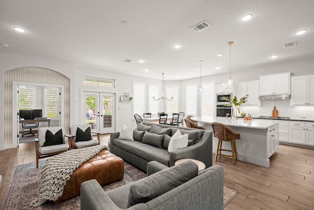 living room featuring french doors, light wood-type flooring, and a chandelier