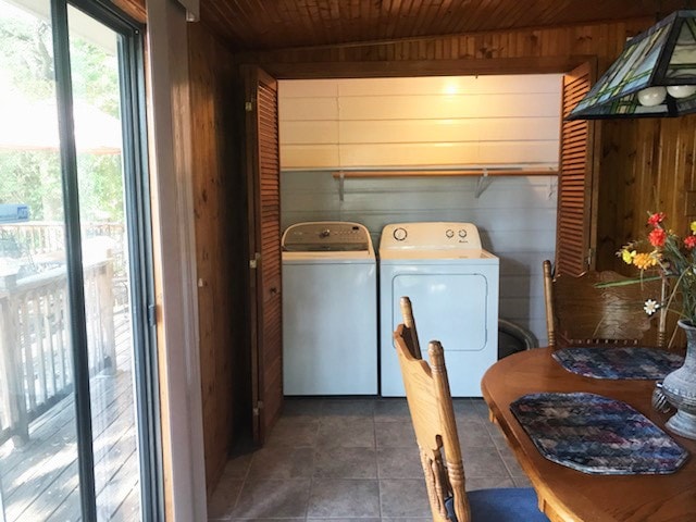 laundry area featuring wood ceiling, washer and dryer, dark tile patterned floors, and wooden walls