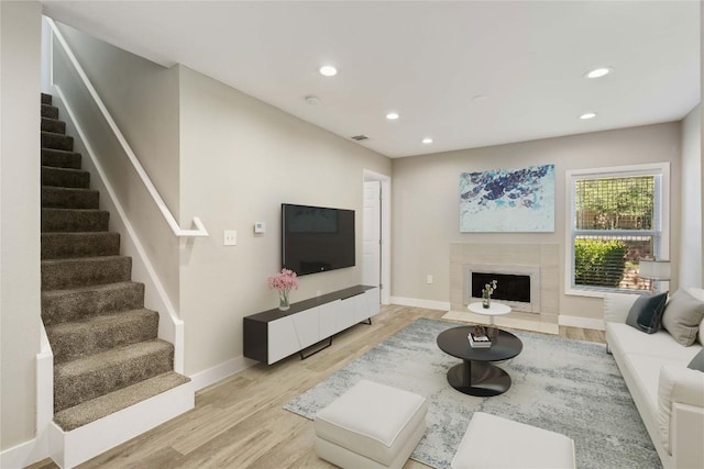 living area with light wood-type flooring, a fireplace with flush hearth, recessed lighting, baseboards, and stairs