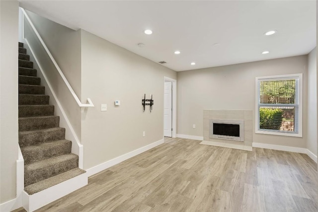 unfurnished living room with a fireplace with flush hearth, light wood-style flooring, recessed lighting, baseboards, and stairs