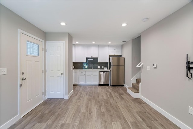 kitchen with stainless steel appliances, baseboards, light wood finished floors, white cabinets, and tasteful backsplash