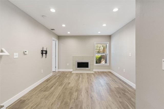 unfurnished living room featuring a tiled fireplace, recessed lighting, baseboards, and light wood finished floors