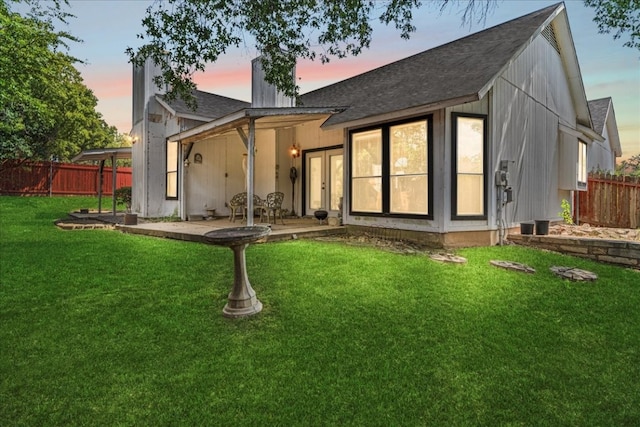 back house at dusk featuring a patio and a yard