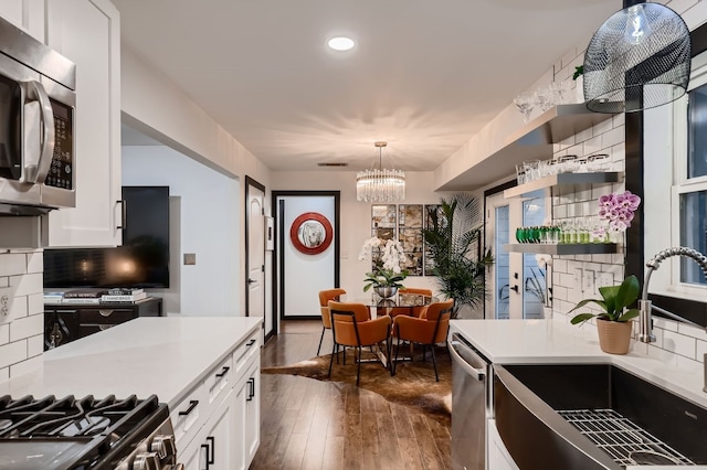 kitchen featuring dark wood-type flooring, white cabinetry, hanging light fixtures, decorative backsplash, and stainless steel appliances