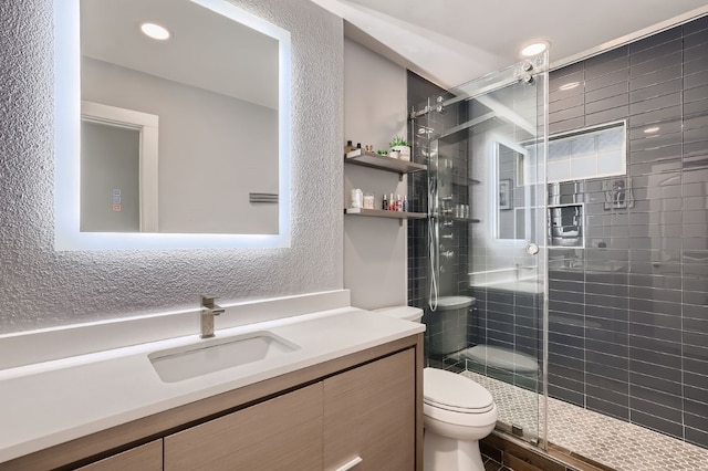 bathroom with a shower with shower door, vanity, and toilet