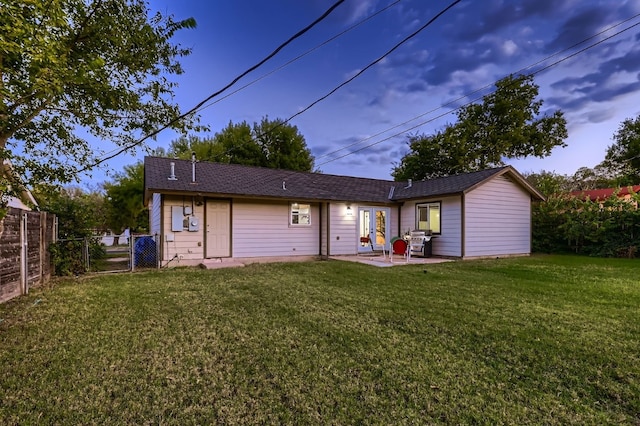 back house at dusk with a patio and a yard