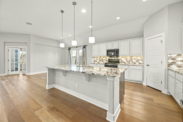 kitchen featuring white cabinets, a center island with sink, light wood-type flooring, and black gas range oven