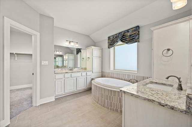 bathroom with tile patterned flooring, vanity, a bath, and vaulted ceiling