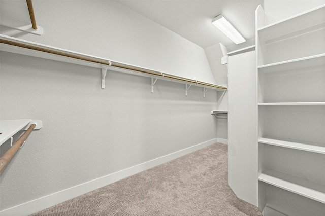 walk in closet with light colored carpet and vaulted ceiling