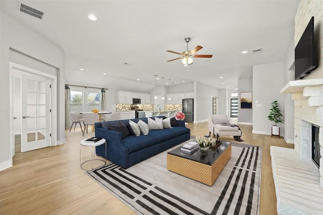 living room featuring ceiling fan, light hardwood / wood-style floors, and a stone fireplace