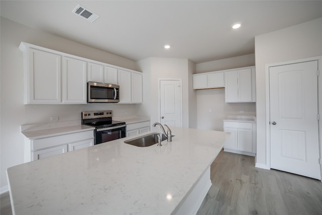 kitchen with sink, light stone countertops, an island with sink, appliances with stainless steel finishes, and white cabinetry