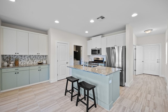 kitchen featuring stainless steel appliances, a center island with sink, white cabinets, backsplash, and a breakfast bar