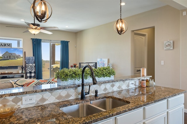 kitchen featuring pendant lighting, sink, white cabinets, backsplash, and dark stone countertops