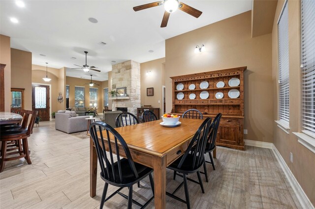 dining space with light hardwood / wood-style flooring, ceiling fan, and a stone fireplace