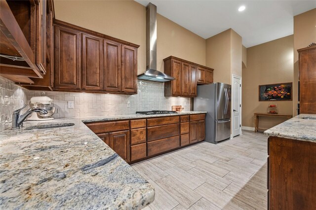 kitchen featuring light stone counters, sink, tasteful backsplash, wall chimney exhaust hood, and stainless steel appliances