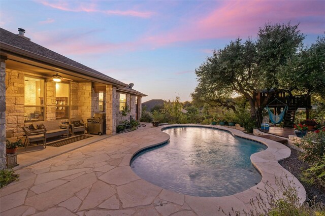 pool at dusk featuring ceiling fan and a patio area