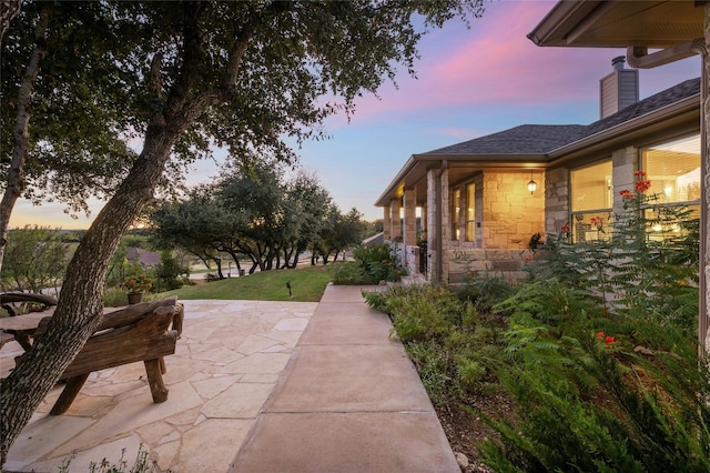 view of home's exterior featuring a patio, stone siding, and roof with shingles