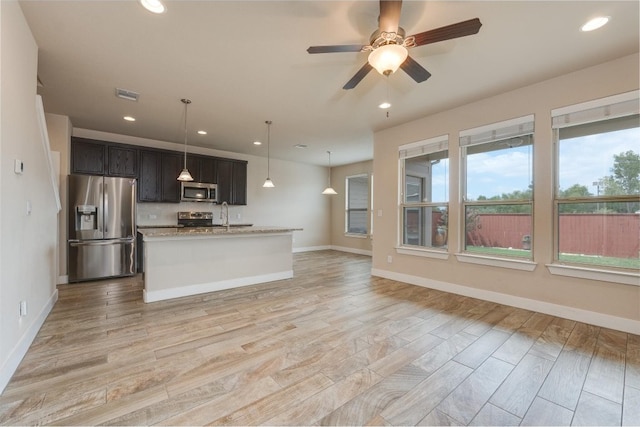 kitchen featuring light stone counters, ceiling fan, a center island with sink, appliances with stainless steel finishes, and light hardwood / wood-style floors