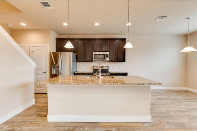 kitchen featuring stainless steel appliances, light stone counters, light wood-type flooring, and a kitchen island with sink