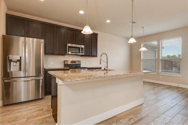 kitchen featuring appliances with stainless steel finishes, light hardwood / wood-style floors, decorative light fixtures, a kitchen island with sink, and sink