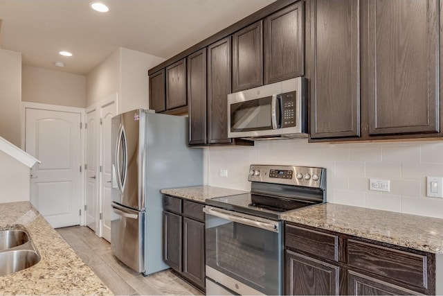 kitchen with appliances with stainless steel finishes, dark brown cabinets, light stone counters, and tasteful backsplash