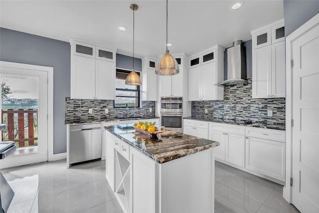 kitchen with pendant lighting, white cabinetry, a kitchen island, wall chimney exhaust hood, and appliances with stainless steel finishes