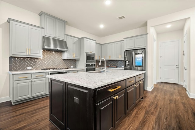 kitchen with appliances with stainless steel finishes, gray cabinetry, dark wood-type flooring, a kitchen island with sink, and sink