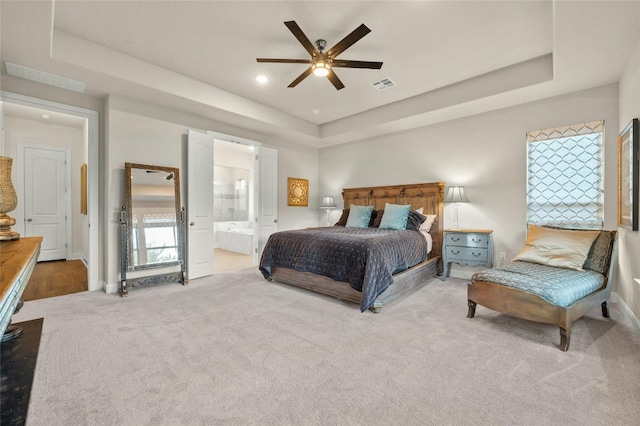 bedroom with light carpet, a tray ceiling, ceiling fan, and ensuite bathroom