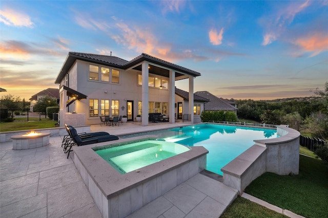 back house at dusk with a patio, an outdoor fire pit, and a pool with hot tub