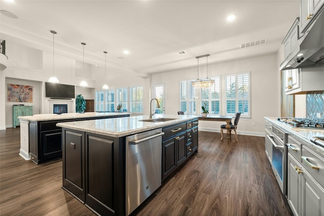 kitchen featuring appliances with stainless steel finishes, hanging light fixtures, an island with sink, dark hardwood / wood-style floors, and sink