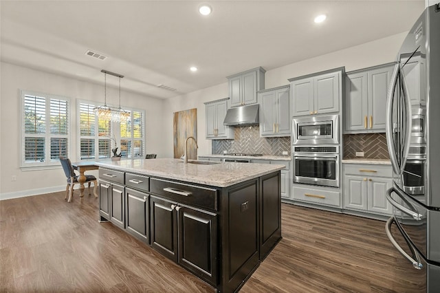 kitchen featuring dark wood-type flooring, sink, gray cabinetry, stainless steel appliances, and a center island with sink