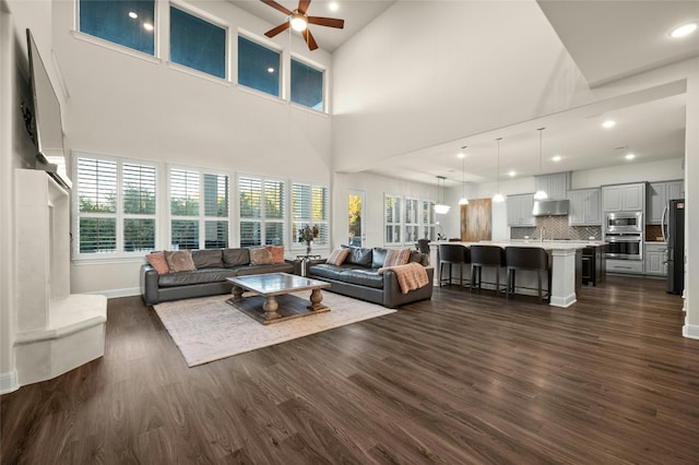 living room with ceiling fan, a high ceiling, and dark hardwood / wood-style flooring