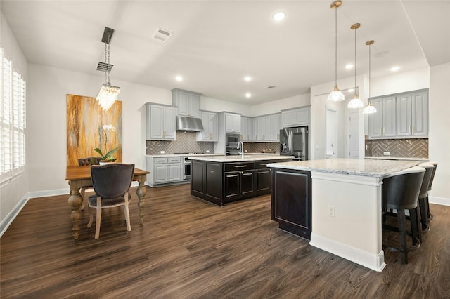 kitchen featuring tasteful backsplash, dark hardwood / wood-style flooring, stainless steel appliances, decorative light fixtures, and a center island with sink