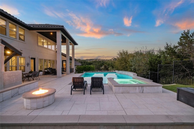 pool at dusk featuring an outdoor living space with a fire pit, an in ground hot tub, and a patio area