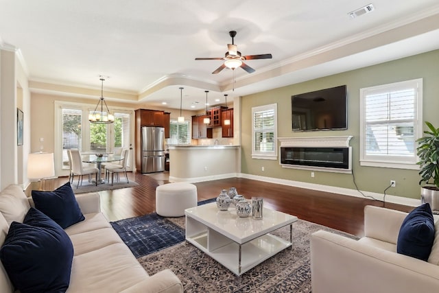 living room featuring hardwood / wood-style floors, ceiling fan with notable chandelier, a healthy amount of sunlight, and a raised ceiling