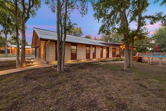 rear view of property with an outdoor pool, stone siding, metal roof, and covered porch