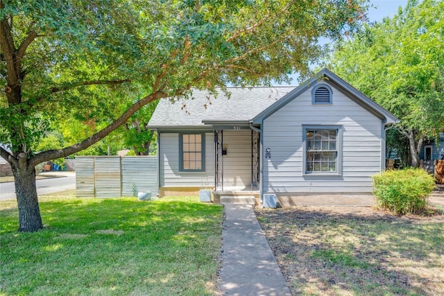 bungalow featuring a front yard, roof with shingles, and fence