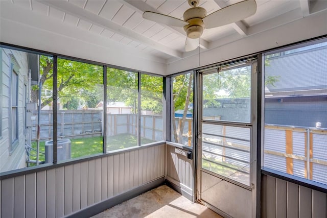 unfurnished sunroom featuring beamed ceiling, a ceiling fan, and a healthy amount of sunlight