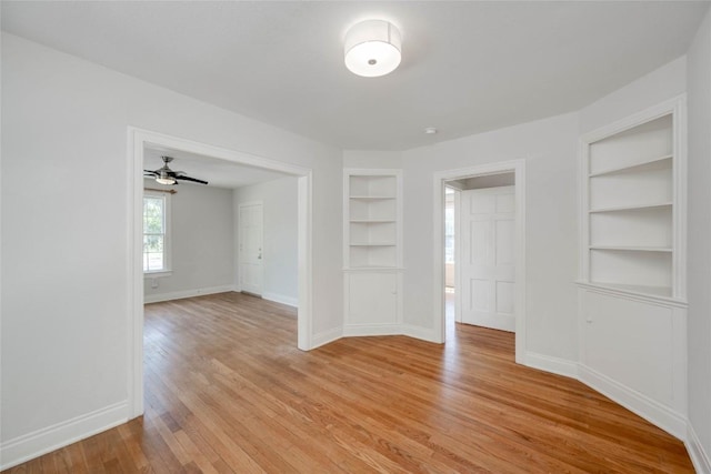 empty room featuring built in shelves, light wood-style flooring, and baseboards