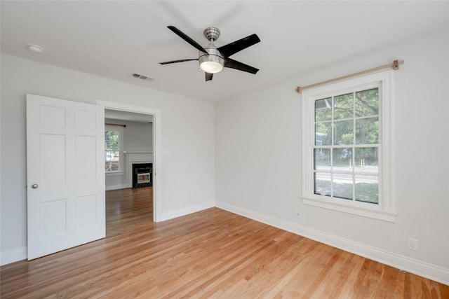 unfurnished room with a wealth of natural light, light wood-type flooring, visible vents, and a fireplace