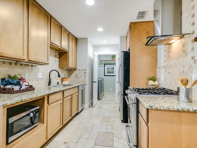 kitchen featuring light stone counters, appliances with stainless steel finishes, wall chimney range hood, and sink