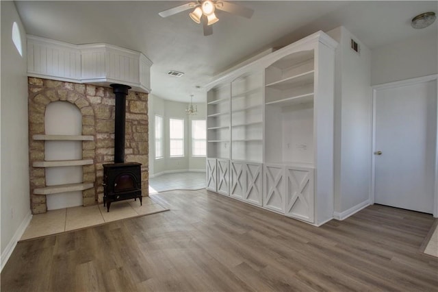 unfurnished living room featuring built in features, hardwood / wood-style floors, ceiling fan, and a wood stove