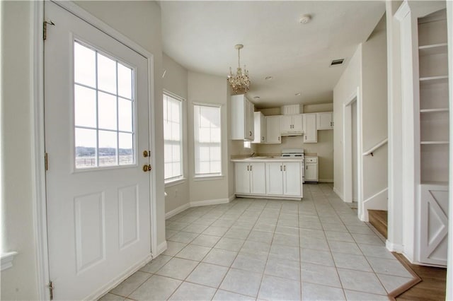 kitchen with hanging light fixtures, light tile patterned floors, white cabinetry, white stove, and a notable chandelier