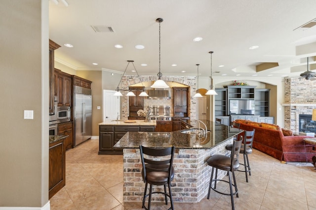 kitchen featuring a large island with sink, backsplash, a breakfast bar, crown molding, and pendant lighting