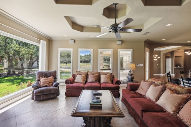 living room with crown molding, light tile patterned flooring, a tray ceiling, and ceiling fan with notable chandelier