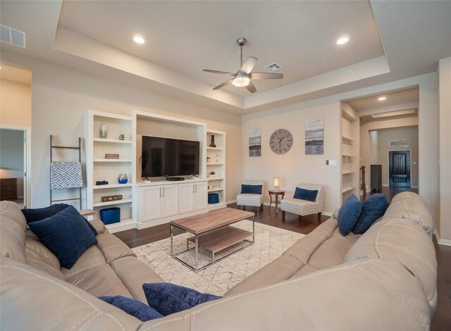 living room featuring wood-type flooring, built in shelves, a tray ceiling, and ceiling fan