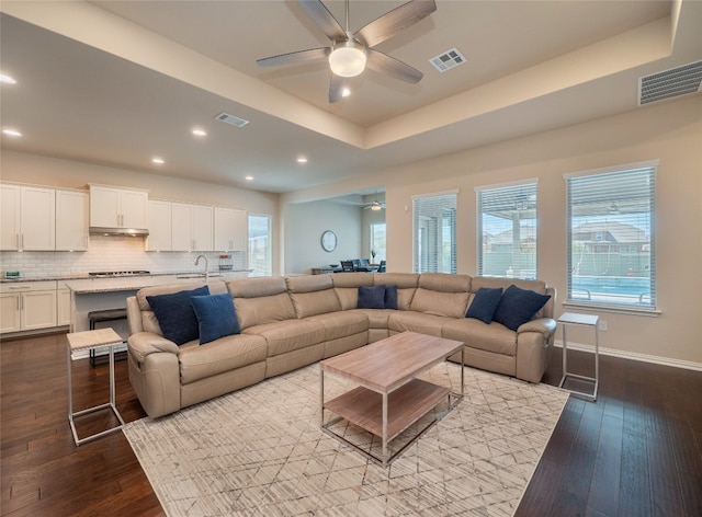 living room featuring light hardwood / wood-style floors, a raised ceiling, ceiling fan, and sink